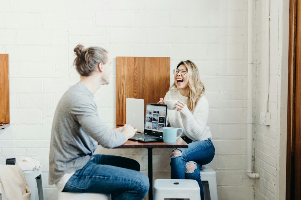 Woman holding a mug and laughing while sitting with a man at a cafe table