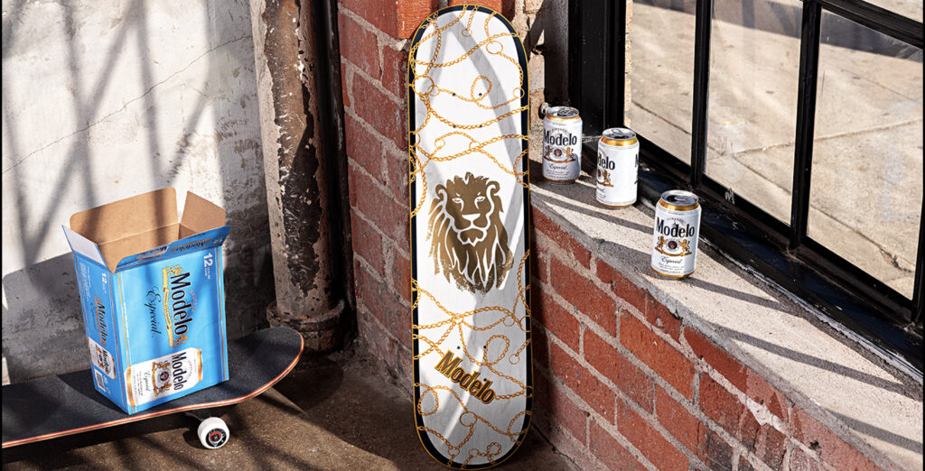 Modelo skateboard leaning up against a wall with cans of Modelo beside it