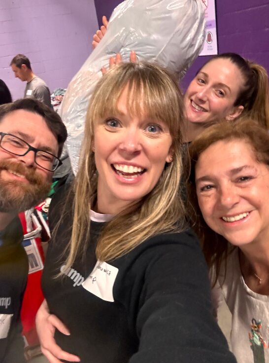 Group of four volunteers smiling for a selfie at a community service event, with one volunteer holding a large bag over their shoulder